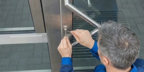 Handwerker in blauer Arbeitskleidung bei der fachgerechten Türöffnung mit Spezialwerkzeug an einer modernen Metalltür.