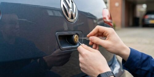 Nahaufnahme von Händen mit Spezialwerkzeug bei der fachgerechten Öffnung eines PKW-Kofferraumschlosses am Tag.